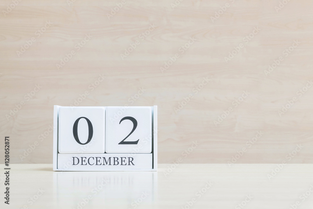 Closeup surface white wooden calendar with black 2 december word on blurred brown wood desk and wood wall textured background with copy space , selective focus at the calendar Closeup surface white wooden calendar with black 2 december word on blurred brown wood desk and wood wall textured background with copy space , selective focus at the calendar