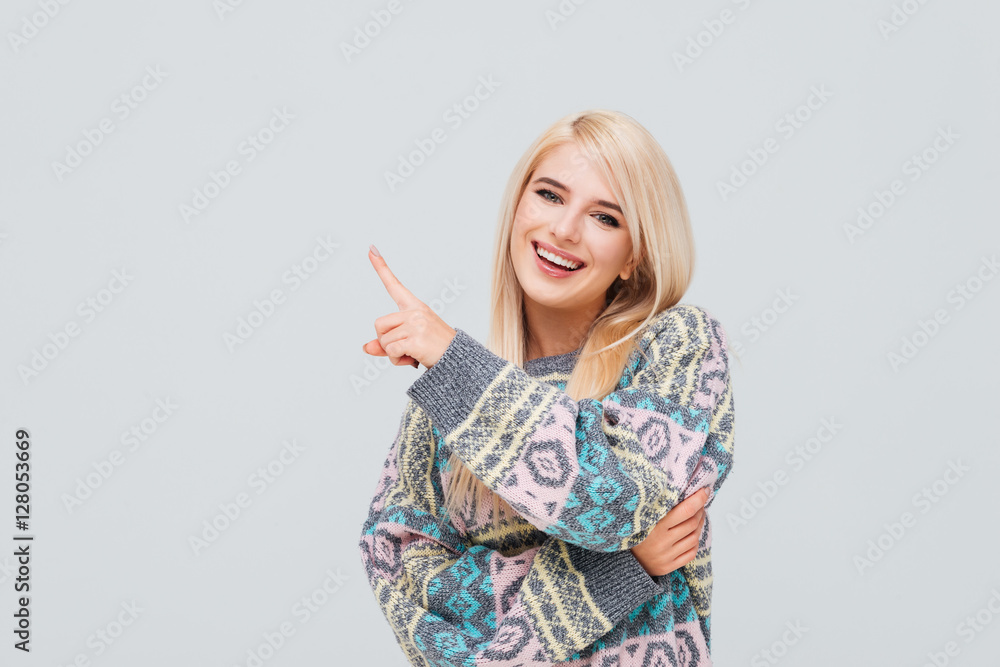 Cheerful young blonde woman in sweater pointing finger away Cheerful young blonde woman in sweater pointing finger away