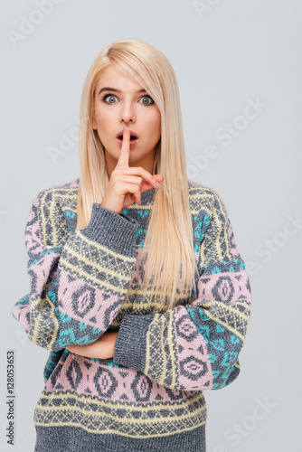 Woman in sweater showing silence gesture with finger over lips photo