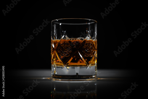 Fotografie A glass of whiskey on the table in dark. Perfect light.