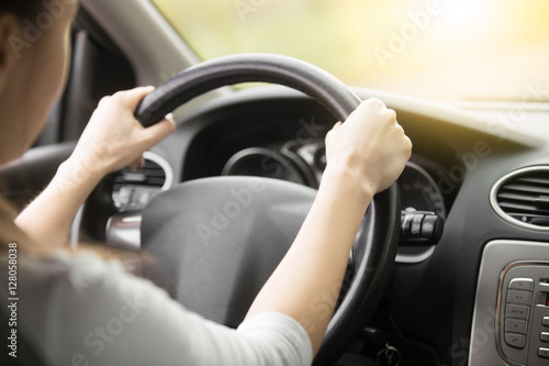 Close up of female hands on the steering. Traveler girl on car trip, looking at the road. View over shoulder