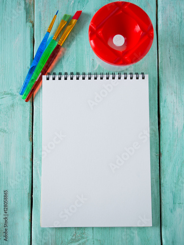 colorful paintbrushes and notebook on wooden surface photo