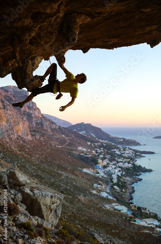 Young man rock climbing in cave at sunset