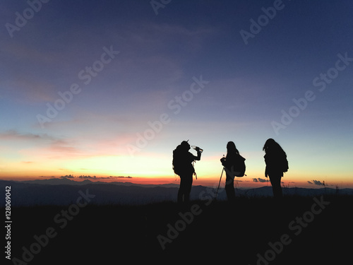 Silhouettes of group hikers people with backpacks enjoying sunset view from top of a mountain. Travel concept, Vintage filtered image. © tirachard