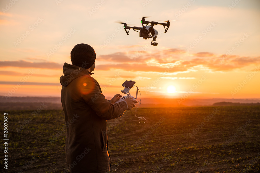 Man operating a drone with remote control. Dark silhouette against colorful sunset. Soft focus. - obrazy, fototapety, plakaty 