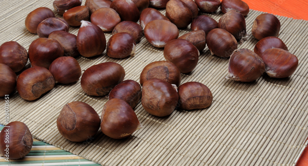 raw chestnuts on bamboo napkin over orange wooden background