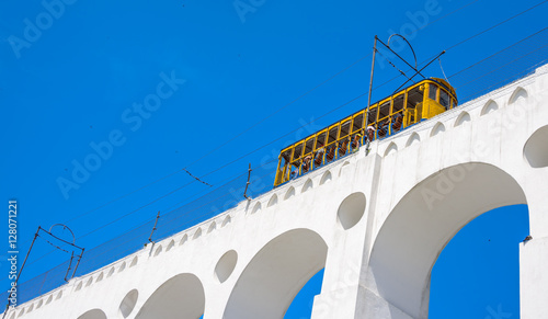 Tram of Santa Tereza, Bonde de Santa Teresa, drives along distinctive white arches, Arcos da Lapa, of the landmark in historic district of Rio de Janeiro - Brazil.