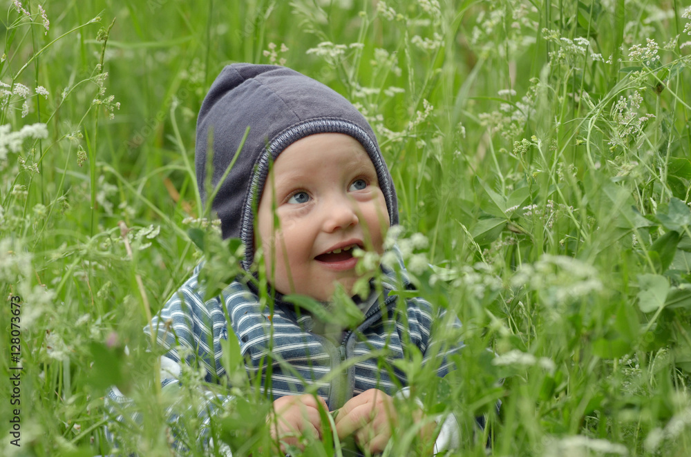Beautiful happy little boy sitting on green meadow with yellow f Beautiful happy little boy sitting on green meadow with yellow f