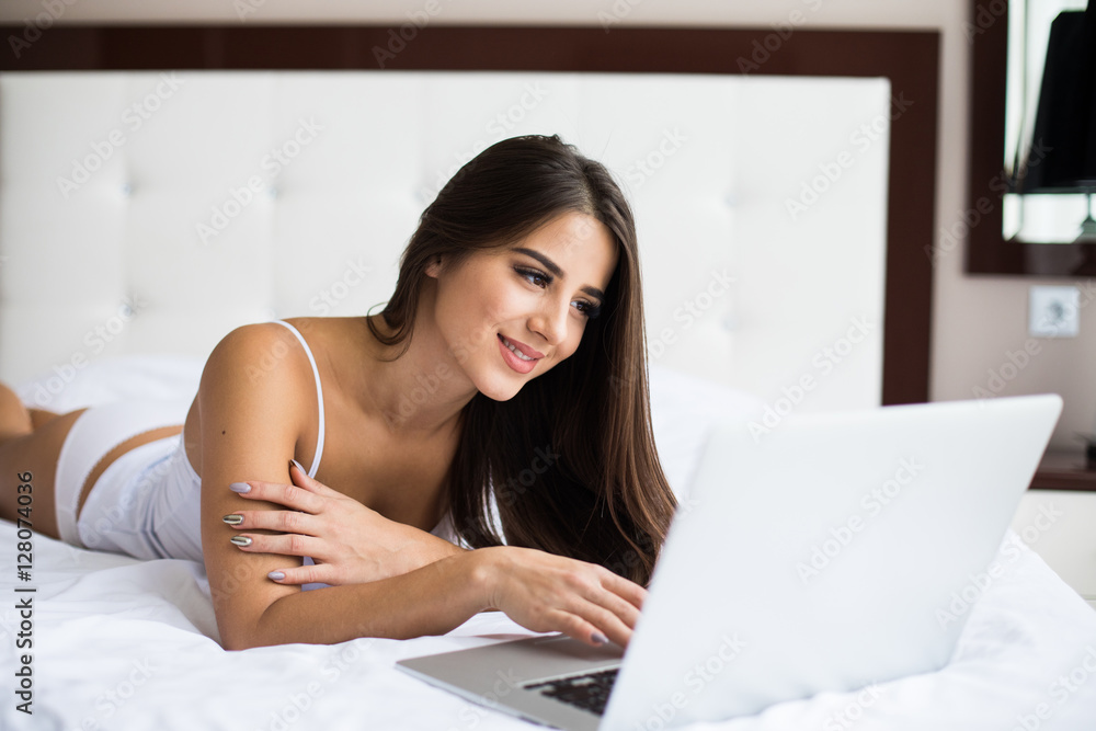 Smiling woman catching up on her social media as she relaxes in bed with a laptop computer on a lazy day