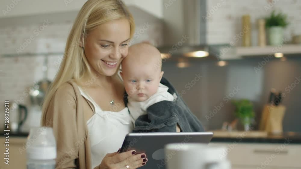 Mother and Her Baby Use Tablet Computer while Being on the Kitchen. Child Touches the Screen. Shot on RED Cinema Camera in 4K (UHD). Mother and Her Baby Use Tablet Computer while Being on the Kitchen. Child Touches the Screen. Shot on RED Cinema Camera in 4K (UHD).