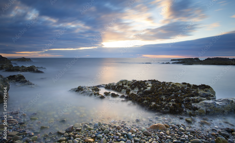 Early morning landscape of ocean over rocky shore with glowing s