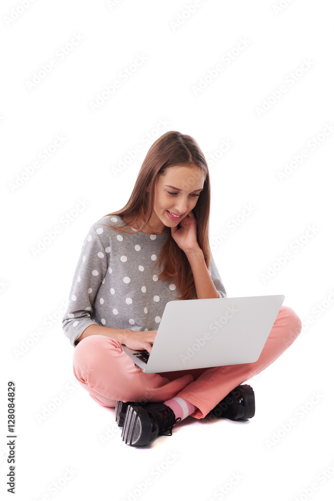 Naklejka premium Side view of happy casual girl sitting on the floor and using la