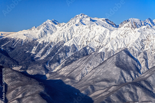 Beautiful mountain winter scenery of the Main Caucasian ridge with snowy peaks on blue sky background © Wilding