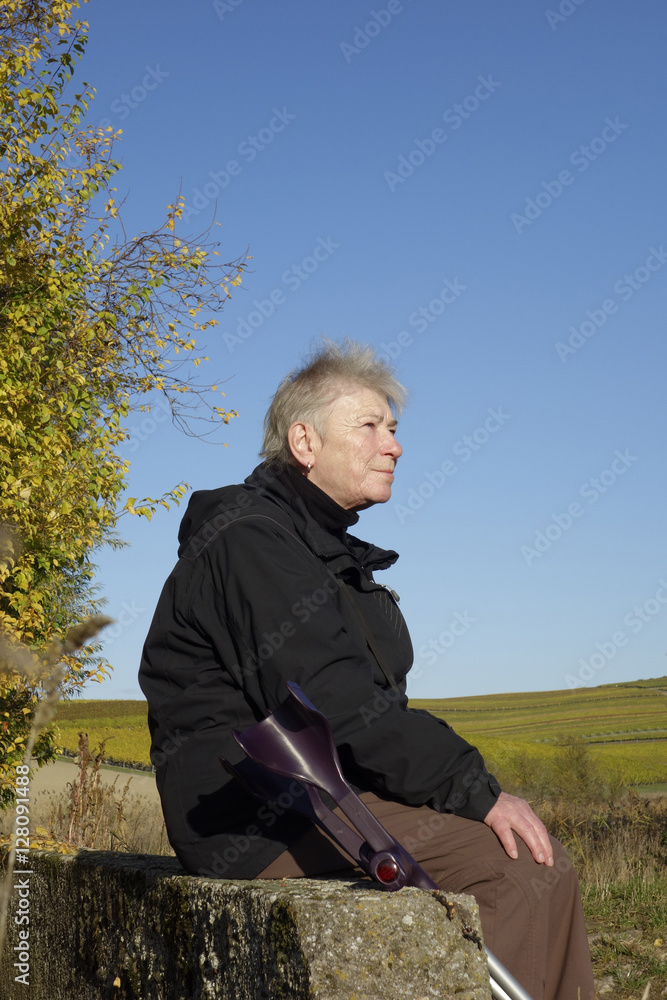 eine seniorin sitzt neben ihren krücken auf einem mäuerchen eine seniorin sitzt neben ihren krücken auf einem mäuerchen