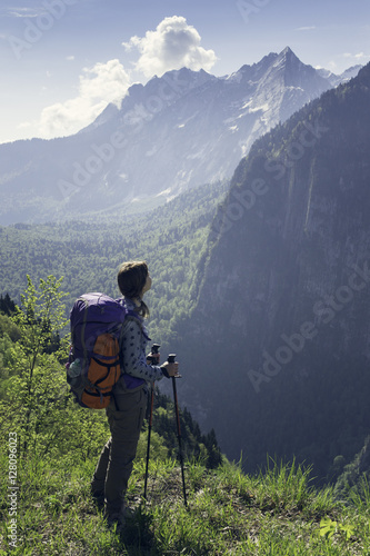 Young positive woman hiking with trekking poles and backpack res