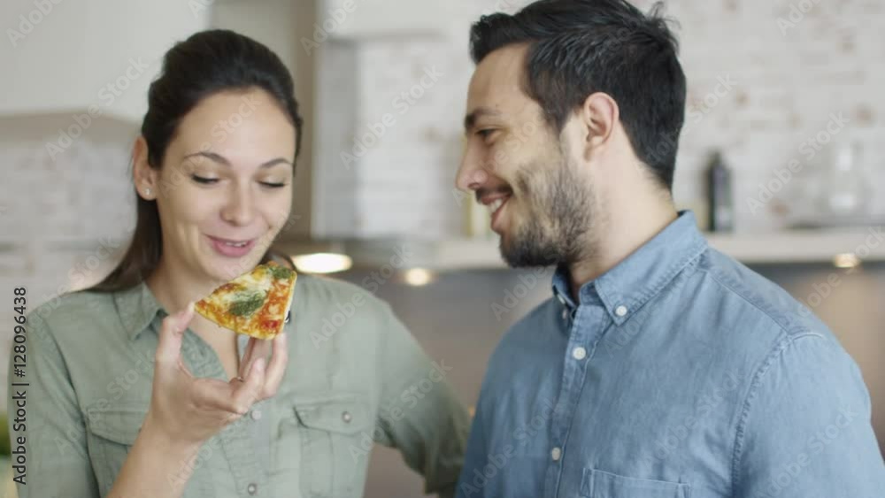 In the Kitchen Young Couple Hungrily and Smilingly Taste Pizza They Have Prepared Themselves. Shot on RED Cinema Camera in 4K (UHD). In the Kitchen Young Couple Hungrily and Smilingly Taste Pizza They Have Prepared Themselves. Shot on RED Cinema Camera in 4K (UHD).