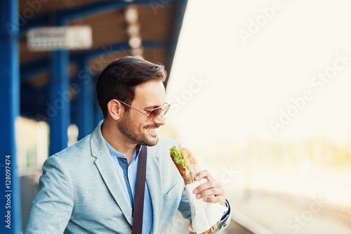Business person is waiting for train and eating sandwich. photo