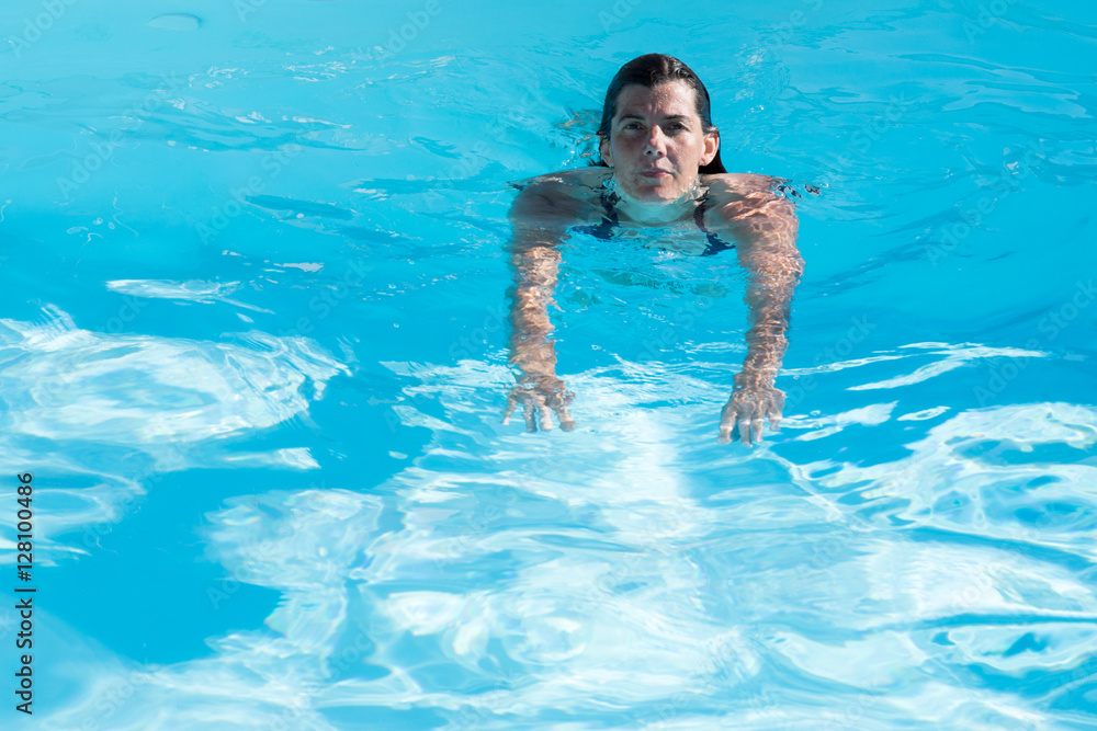 Brunette girl in blue swimming suit swim in blue water