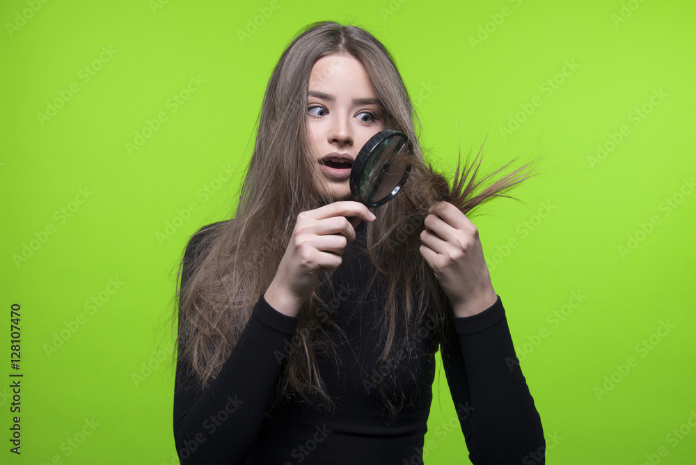 Obraz premium dry and damaged hair ends girl holding magnifier, isolated on green screen