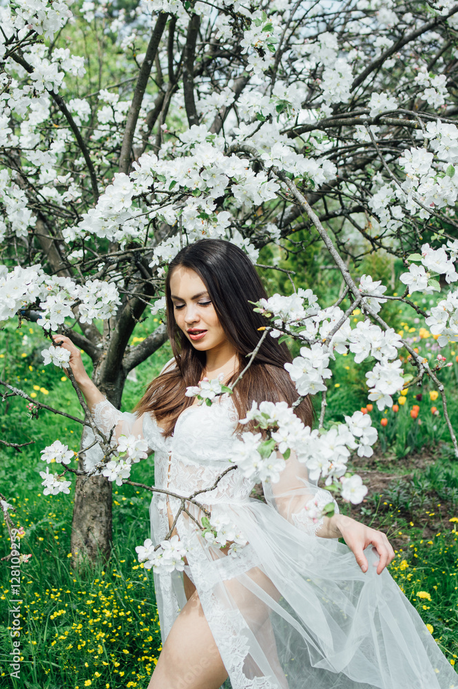 Portrait of young girl in white dress in blossom apple garden, holding dress by hand Portrait of young girl in white dress in blossom apple garden, holding dress by hand