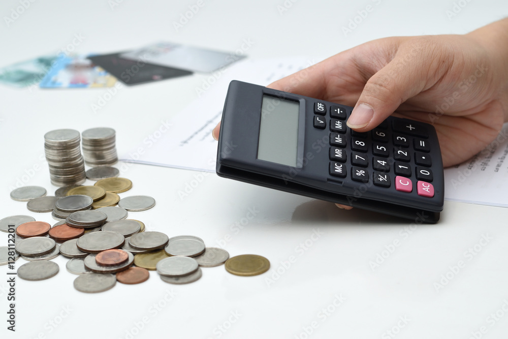 A business man hand using the calculator with coin stacks and financial report on the table A business man hand using the calculator with coin stacks and financial report on the table