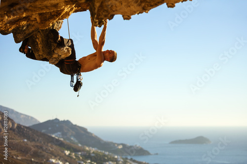 Young man climbing on roof in cave, view of coast below