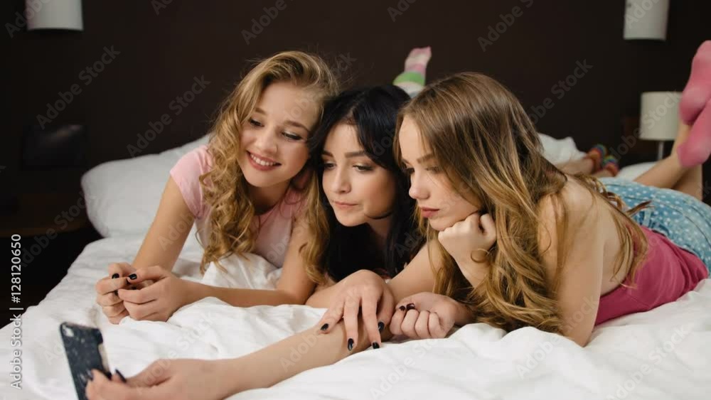 Attractive young ladies taking selfies on the bed in a modern bedroom. Attractive young ladies taking selfies on the bed in a modern bedroom.