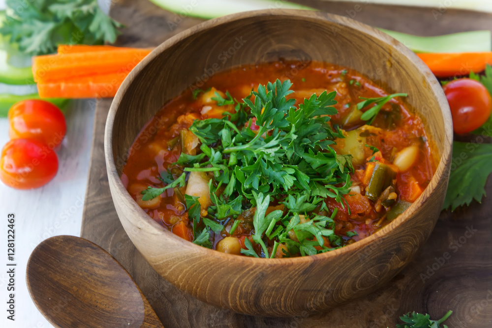 Vegetarian soup in wooden bowl on wood board on white table