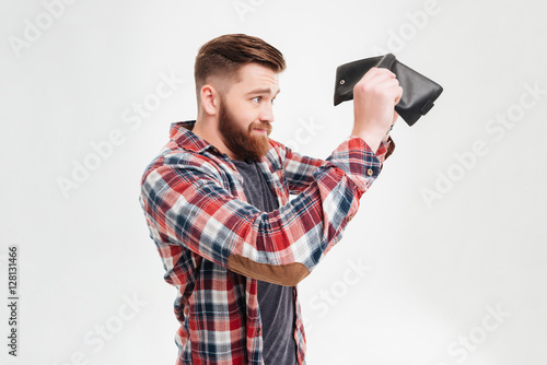 Canvas Print Young man in plaid shirt looking inside his empty wallet