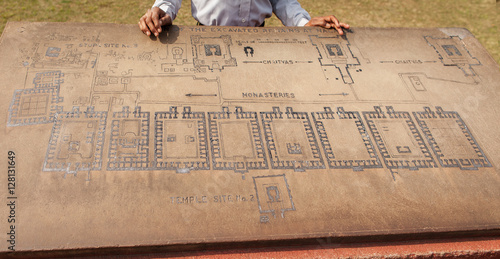 Archaeological heritage of India, ruins of university of Nalanda. Stone with the scheme of excavation. The hands of the Indian guide and plan of territory.