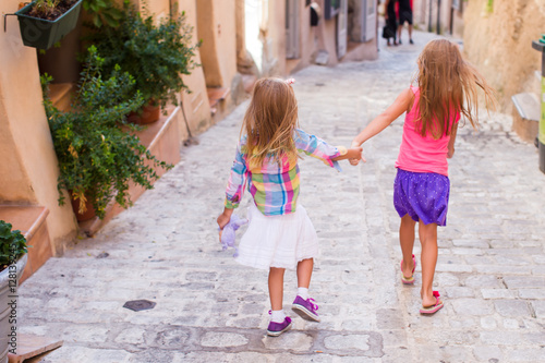 Adorable happy little girls outdoors in narrow street at small city