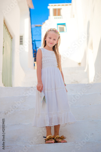 Adorable girl outdoors in greek village. Kid at street of typical greek traditional village with white stairs on greek island