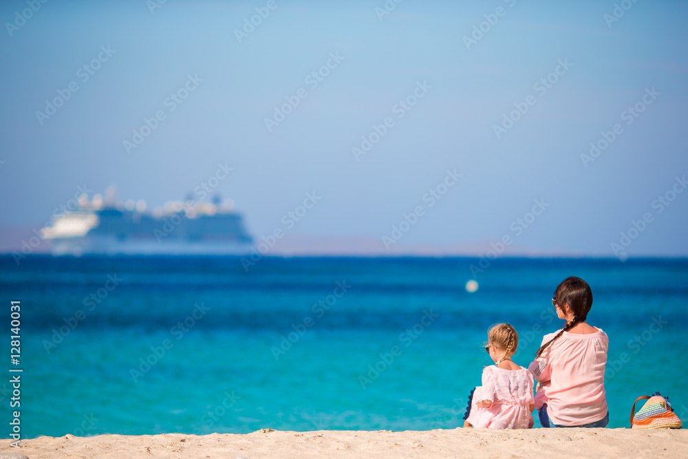 Young mom and adorable girl at beach on sunny day with view of big liner