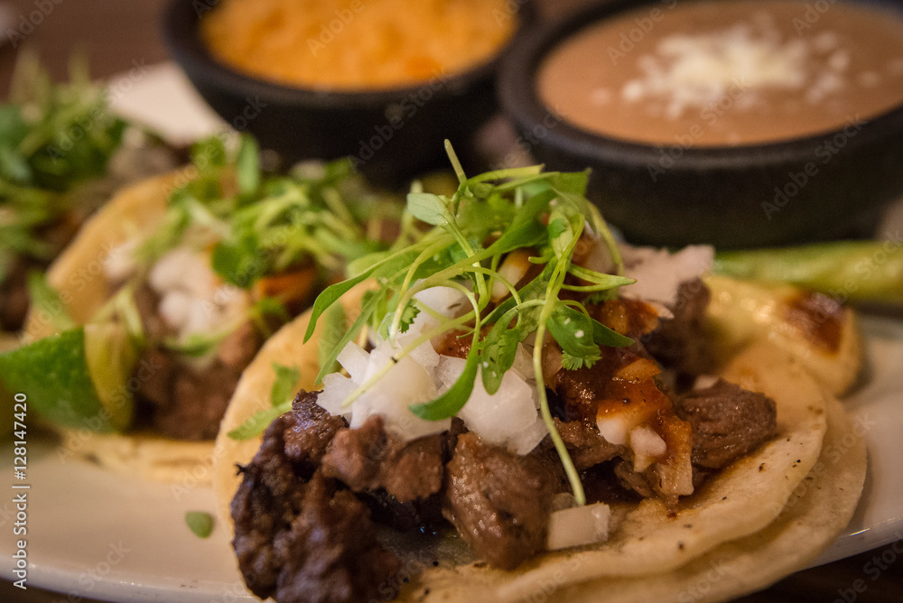 Plate of three street style tacos topped with micro greens, onions, chives and various sides Plate of three street style tacos topped with micro greens, onions, chives and various sides