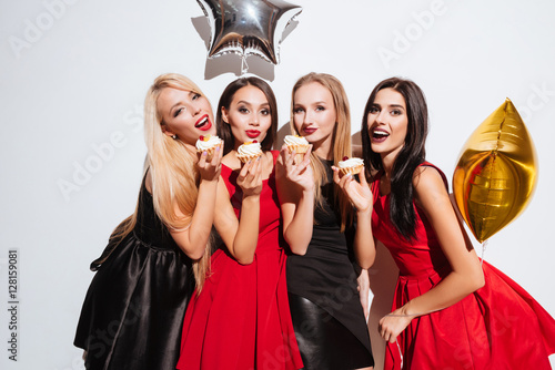 Four happy women standing and eating cupcakes on the party photo