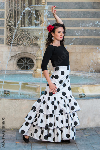 Young beautiful woman in a flamenco costume. Fountain on the background. 