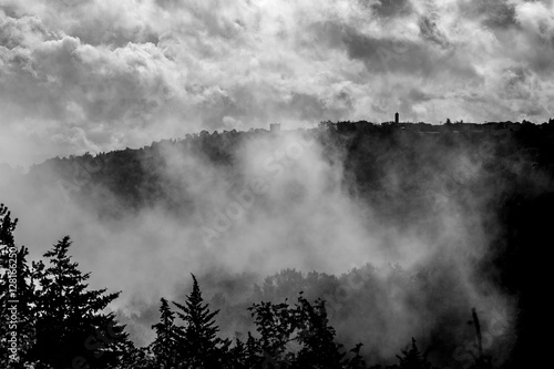 Mist, fog and clouds above the old town.  The weather changes dynamically above Tuscany, Italy. Road view. © lightcaptured