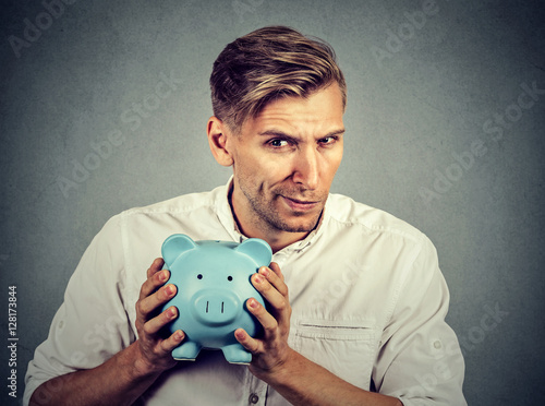 Young greedy stingy business man holding piggy bank photo