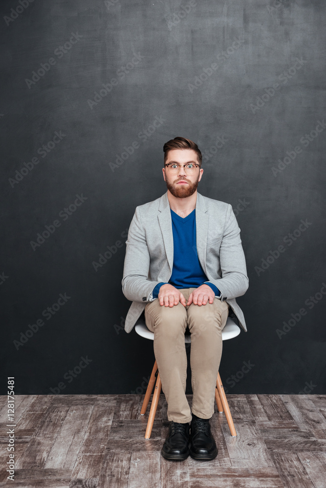 Serious bearded young man nerd in glasses sitting on chair