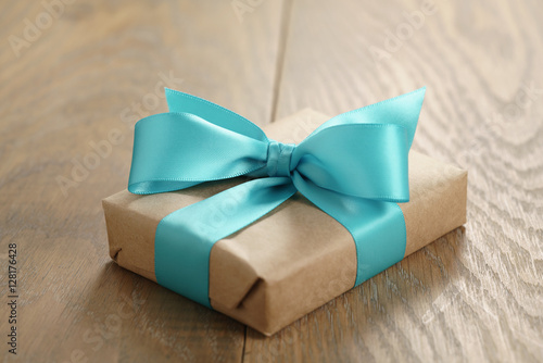 rustic craft paper gift box with blue ribbon bow on wood table, shallow focus