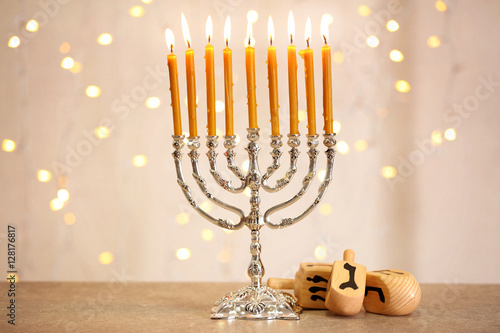 Menorah with dreidels for Hanukkah on table against defocused lights