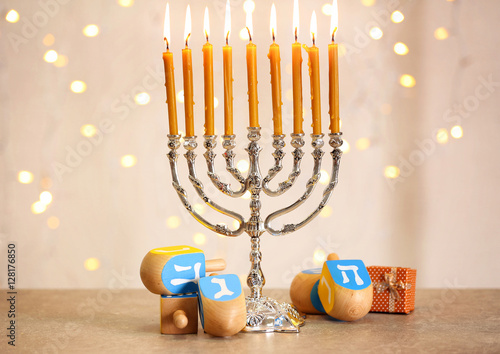 Menorah with dreidels for Hanukkah on table against defocused lights
