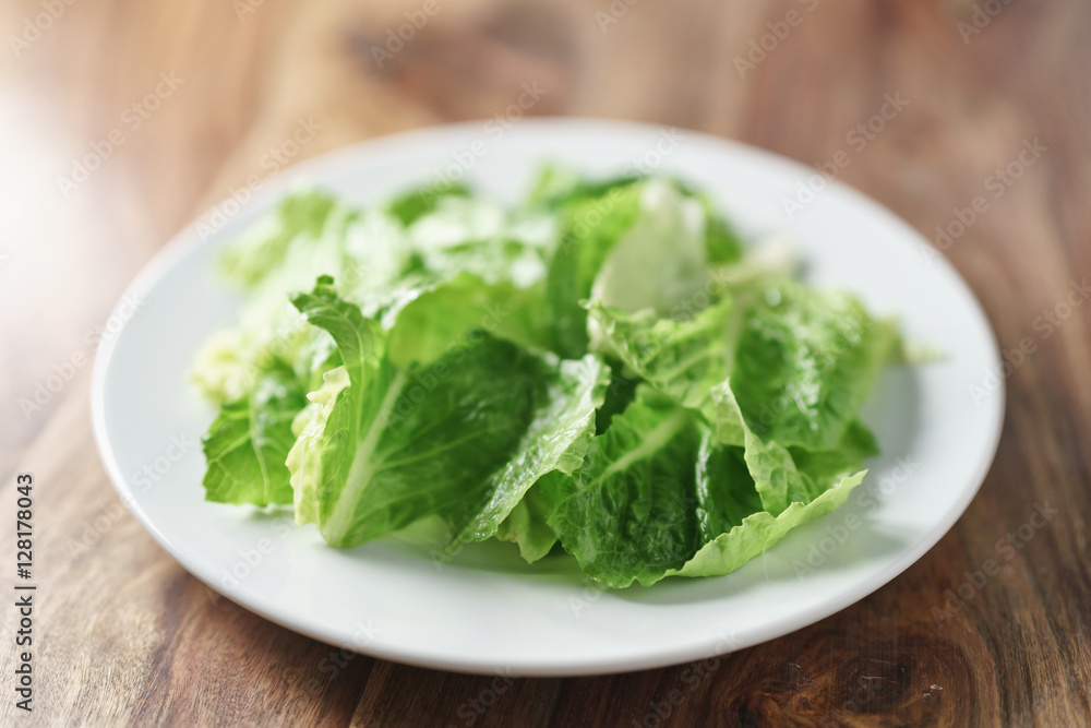 torn romaine lettuce leaves in plate on wood table, diet food torn romaine lettuce leaves in plate on wood table, diet food