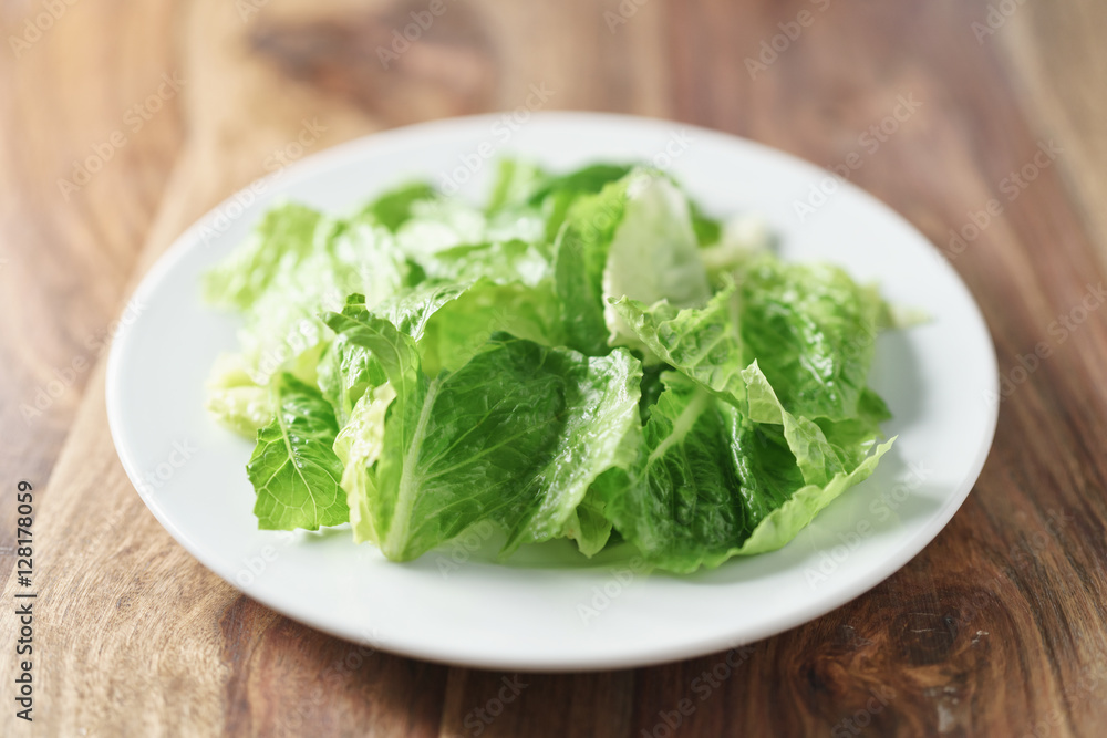torn romaine lettuce leaves in plate on wood table, diet food torn romaine lettuce leaves in plate on wood table, diet food