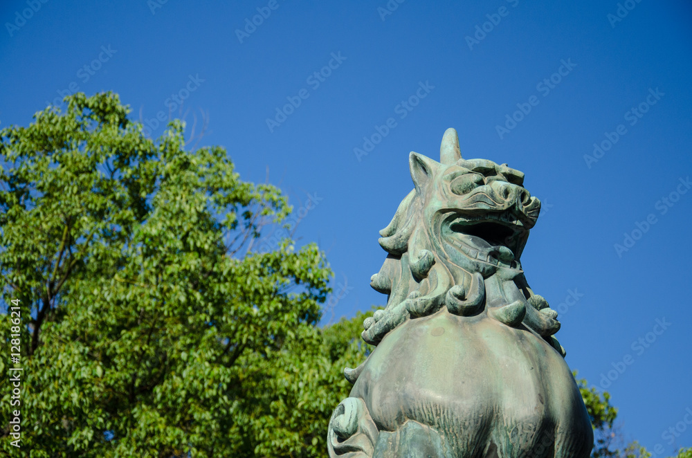 Close Up Ancient Iron or Bronze Stucco Japanese Traditional Lion God Handmade with Blue Sky and Tree Background Wallpaper.Lion Statue famous to build in the Temple in Japan