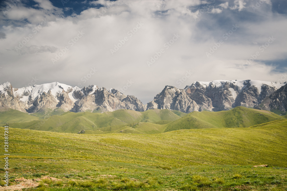 At-Bashi Mountain peaks with snow, green pastures under cloudy sky in Kyrgyzstan