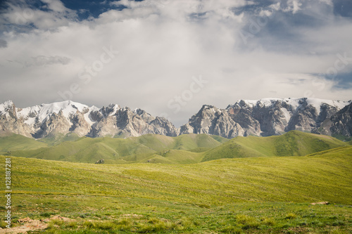 At-Bashi Mountain peaks with snow, green pastures under cloudy sky in Kyrgyzstan photo