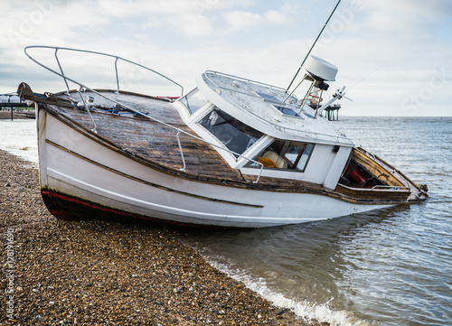 A beached boat flooded on a pebbled beach. There is water in the back of the boat as it is sinking.