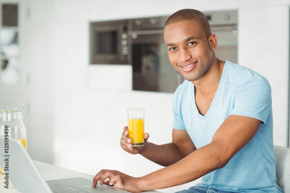 Smiling man using laptop and drinking orange juice