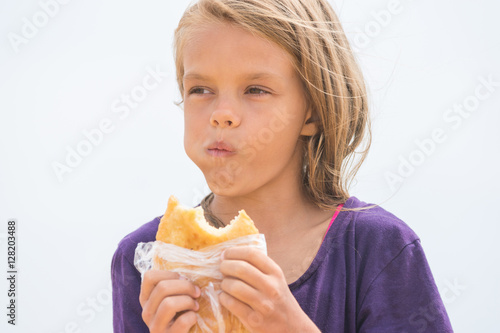 A hungry girl with an appetite chews delicious cake on the beach